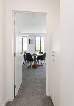 A hallway leading to a dining area with a table and chairs, carpeted floor, and a white door. - Luxe 1BR City Apt | Modern, Spacious w/ Parking (Wellington)
