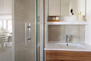 A modern bathroom with a glass shower enclosure, a white sink with a wooden vanity, and a mirror above the sink. - Luxe 1BR City Apt | Modern, Spacious w/ Parking (Wellington)