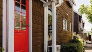 A two-story house with a red door and white trim, a small front porch, and a visible air conditioning unit.