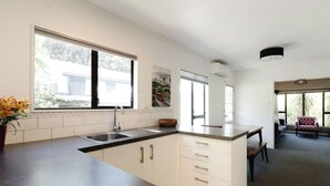 A modern kitchen with a large island, white cabinetry, and a view of the outdoors through large windows.