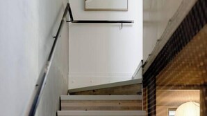A staircase with wooden steps and a metal handrail, leading to a room with a large window and a hanging light fixture. - Executive 2BR Designer Townhouse + Rooftop Oasis (Wellington)