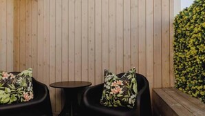 A wooden deck with two black chairs and a small round table, surrounded by wooden walls and a green hedge. - Executive 2BR Designer Townhouse + Rooftop Oasis (Wellington)