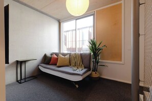 Ein gemütliches Zimmer mit einer Couch, einem kleinen Tisch, einer Topfpflanze und einem großen Fenster.