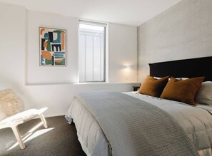 Ein Schlafzimmer mit einem Bett, einem Sessel, einem Fenster und einem Wandbild.
