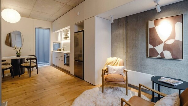 A modern living room with a sofa, a round rug, and a dining area with a table and chairs. - Executive 2BR Designer Townhouse + Rooftop Oasis (Wellington)
