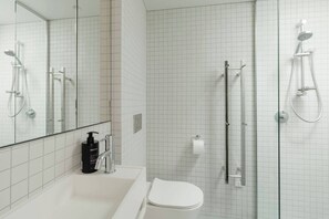Ein modernes Badezimmer mit einer weißen Duschkabine, einer separaten Dusche mit Glastüren, einem weißen Waschbecken inklusive Seifenspender und einer Toilette.