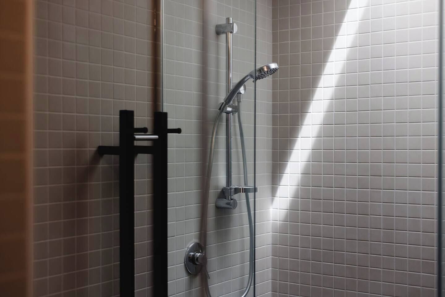 A shower with a handheld showerhead and a wall-mounted control valve.