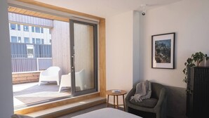A hotel room with a large bed, a small round table, a gray armchair, a sliding glass door leading to an outdoor deck with white chairs, and a framed picture on the wall. - Urban Oasis | Spacious 3BR Townhouse w Terrace (Wellington)