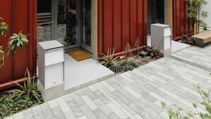 A modern building with a red facade, large windows, and a small outdoor seating area with plants. - Urban Oasis | Spacious 3BR Townhouse w Terrace (Wellington)