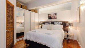 A bedroom with a large bed, bedside lamps, a mirror, and a wooden floor.