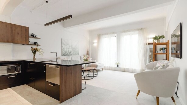 A modern kitchen with dark cabinetry, a central island, and a dining area with a white sofa and a round table.