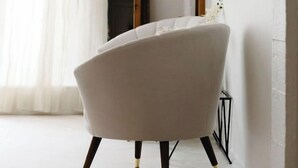 A modern living room with a white armchair, a wooden sideboard with plants, and a wall-mounted mirror.