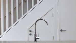 A modern kitchen with a stainless steel sink, a white door, and a staircase with white railings. - Chic 2BR Apartment | Secure Gated Complex in CBD (Wellington)