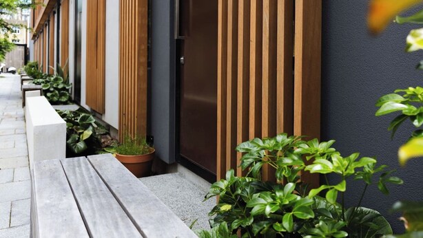 A modern building with a wooden slatted wall, a concrete bench, and potted plants. - Chic 2BR Apartment | Secure Gated Complex in CBD (Wellington)
