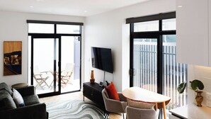 A modern living room with a sofa, a coffee table, a TV, and a balcony with a view. - Chic 2BR Apartment | Secure Gated Complex in CBD (Wellington)