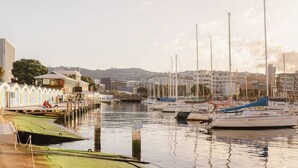 Un port de plaisance avec des bateaux amarrés, une jetée où se promènent des gens, et des bâtiments en arrière-plan.