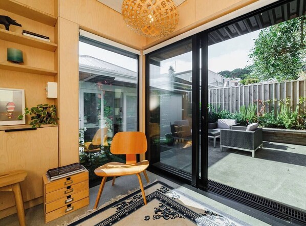 Un intérieur moderne avec un bureau en bois, une chaise et une grande porte-fenêtre coulissante donnant sur un patio extérieur aménagé avec du mobilier.