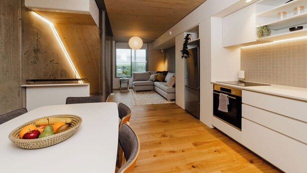 A modern kitchen with white cabinetry, a wooden floor, and a dining area with a table set for two. - Spacious 2BR Oasis in Central Wellington w Terrace (Auckland)