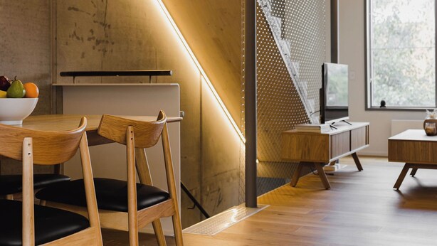 Un intérieur moderne avec un plancher en bois, un escalier et un coin repas agrémenté d’un saladier de fruits.