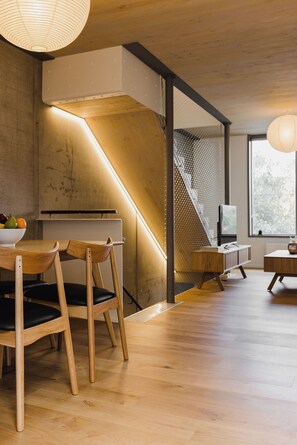 A modern interior with wooden flooring, a staircase, and a dining area with a bowl of fruit. - Urban Chic | 2BR Central Apartment (Wellington)
