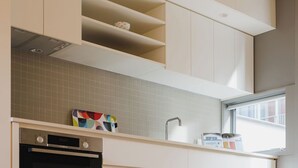 Une cuisine moderne avec des meubles blancs, un four encastré et une fenêtre qui laisse entrer la lumière naturelle.