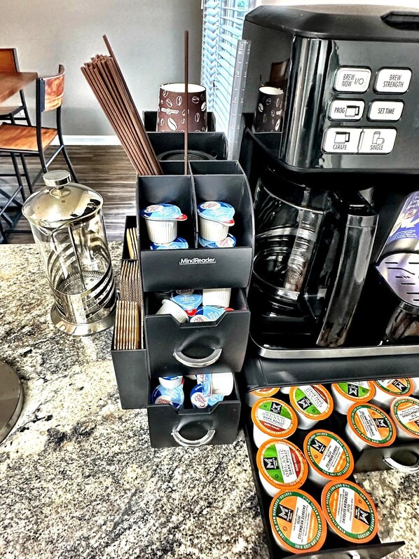 A coffee station with a coffee maker, a grinder, and a dispenser with coffee pods. - Southern Solace (Newnan)