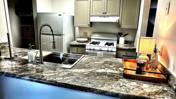 A compact kitchen with a stainless steel sink, a gas stove, and light-colored cabinets. - Southern Solace (Newnan)