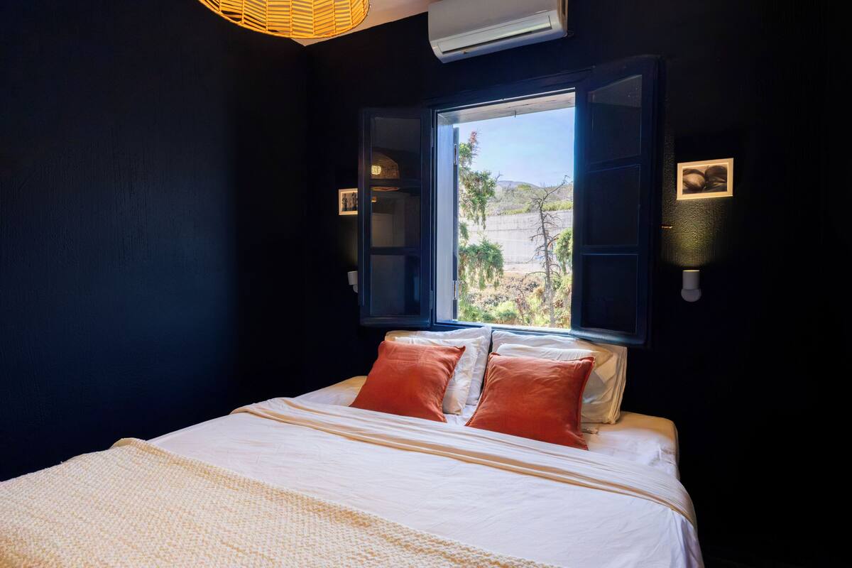 A bedroom with a bed, a window, and a wall-mounted air conditioner.