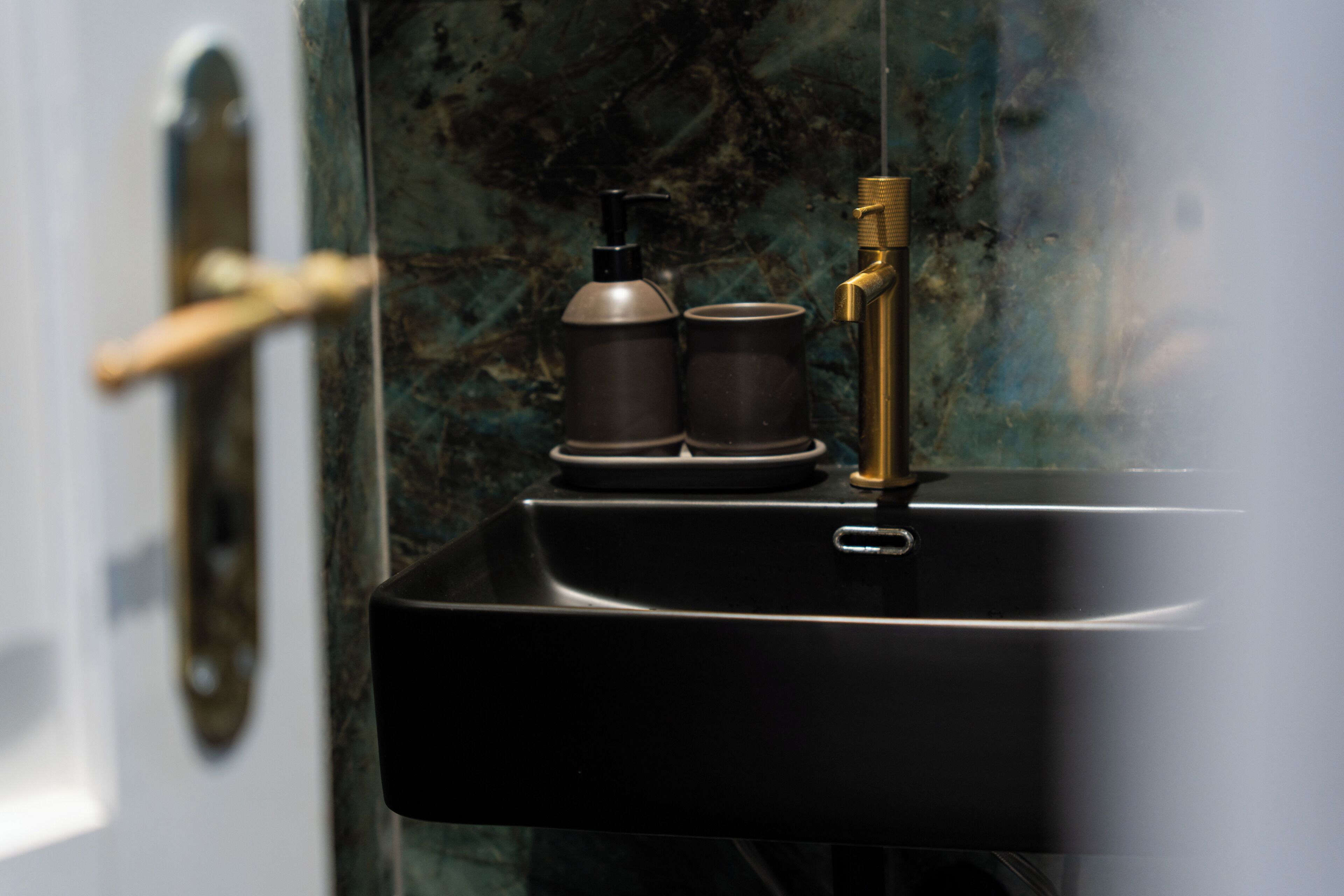 A bathroom sink with a black basin, a gold faucet, and two black bottles on the countertop.