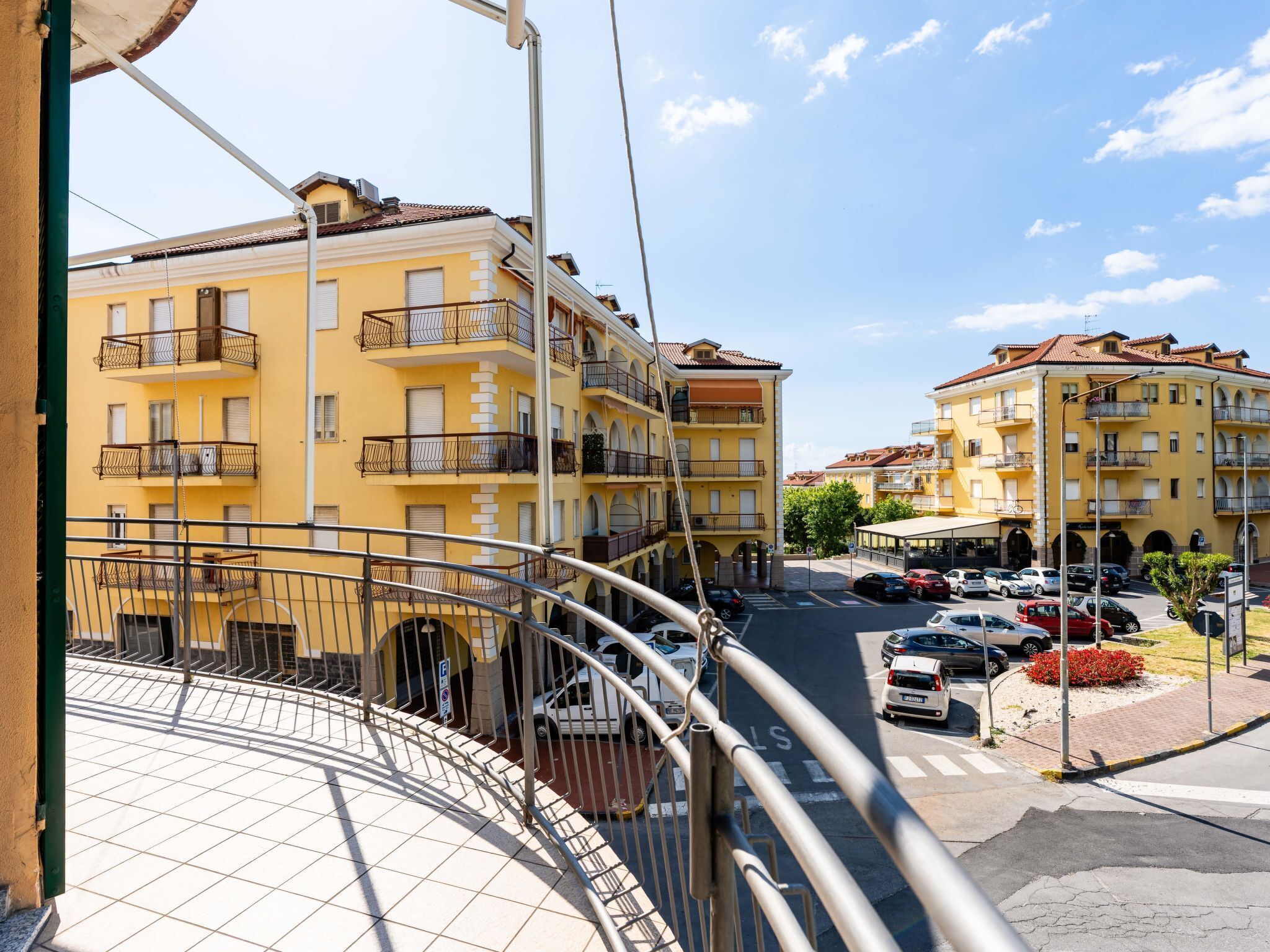 A yellow building with balconies and a parking area in front.