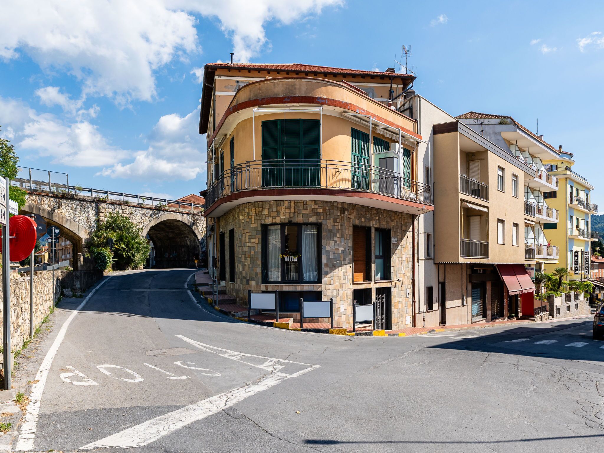 A multi-story building with a curved facade, balconies, and a stone bridge in the background.