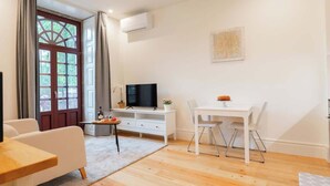 Un salon moderne avec un plancher en bois, un canapé blanc, une table à manger avec des chaises, un téléviseur et une fenêtre avec des rideaux.