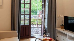 Une pièce avec une grande fenêtre, un téléviseur, une petite table avec une bouteille et des verres, et un canapé.