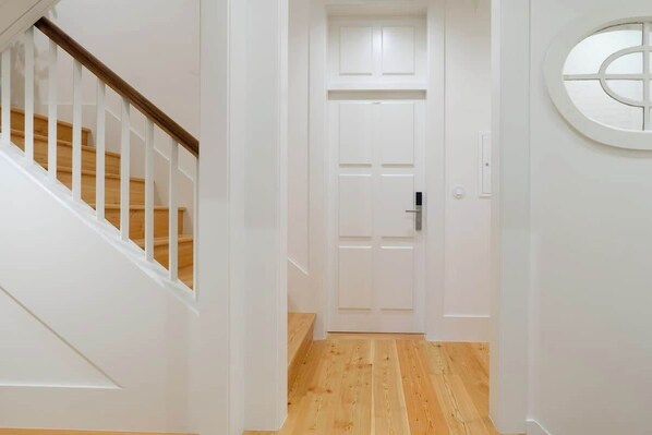 A hallway with a wooden staircase, a white door with a keyhole, and a round window on the wall.