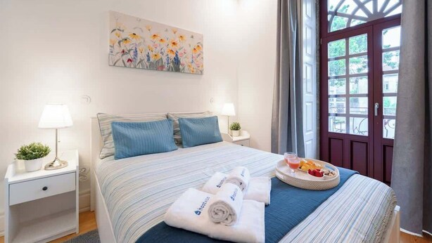 Une chambre d’hôtel avec un lit, un tableau au mur, une fenêtre avec des rideaux et un plateau de petit-déjeuner posé sur le lit.