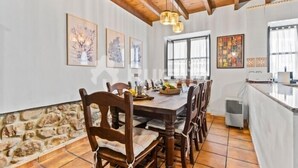 A dining area with a wooden table and chairs, a stone wall, and artwork on the walls. - La Casina del Rincón - country house in Riocaliente (Llanes) (Jareras)