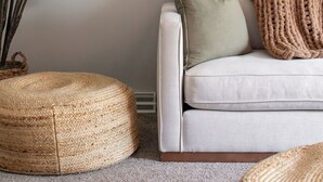 Ein Wohnzimmer mit einem weißen Sofa, einer gestrickten Decke, einem grünen Kissen und einer großen Topfpflanze.
