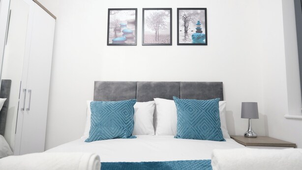 Une chambre à coucher avec un lit, des oreillers, une table de chevet, une lampe et trois tableaux encadrés accrochés au mur.