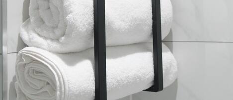 A black towel rack holding four neatly rolled white towels against a white tiled wall.