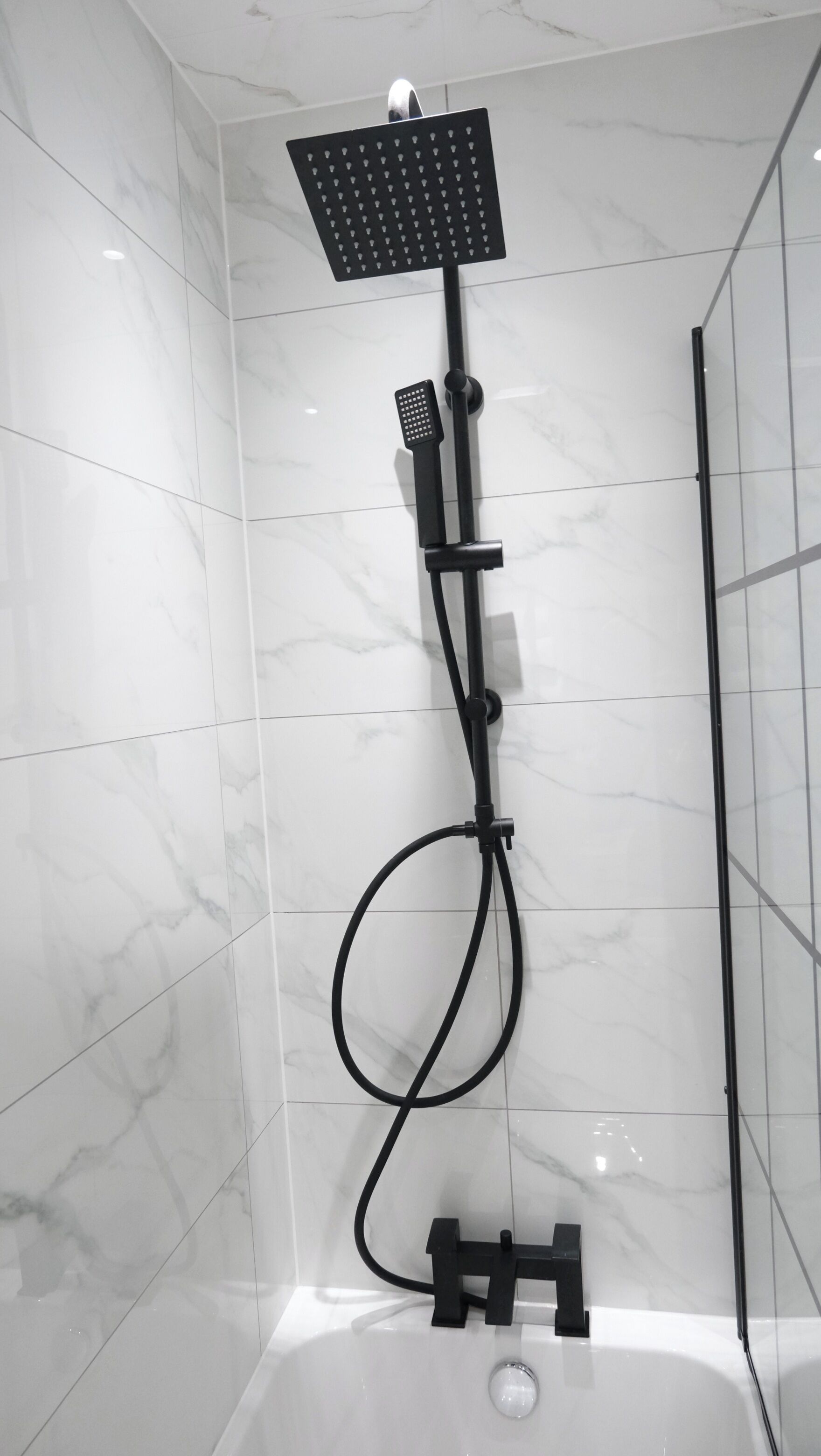 A modern bathroom with a black shower system, a handheld showerhead, and a bathtub.