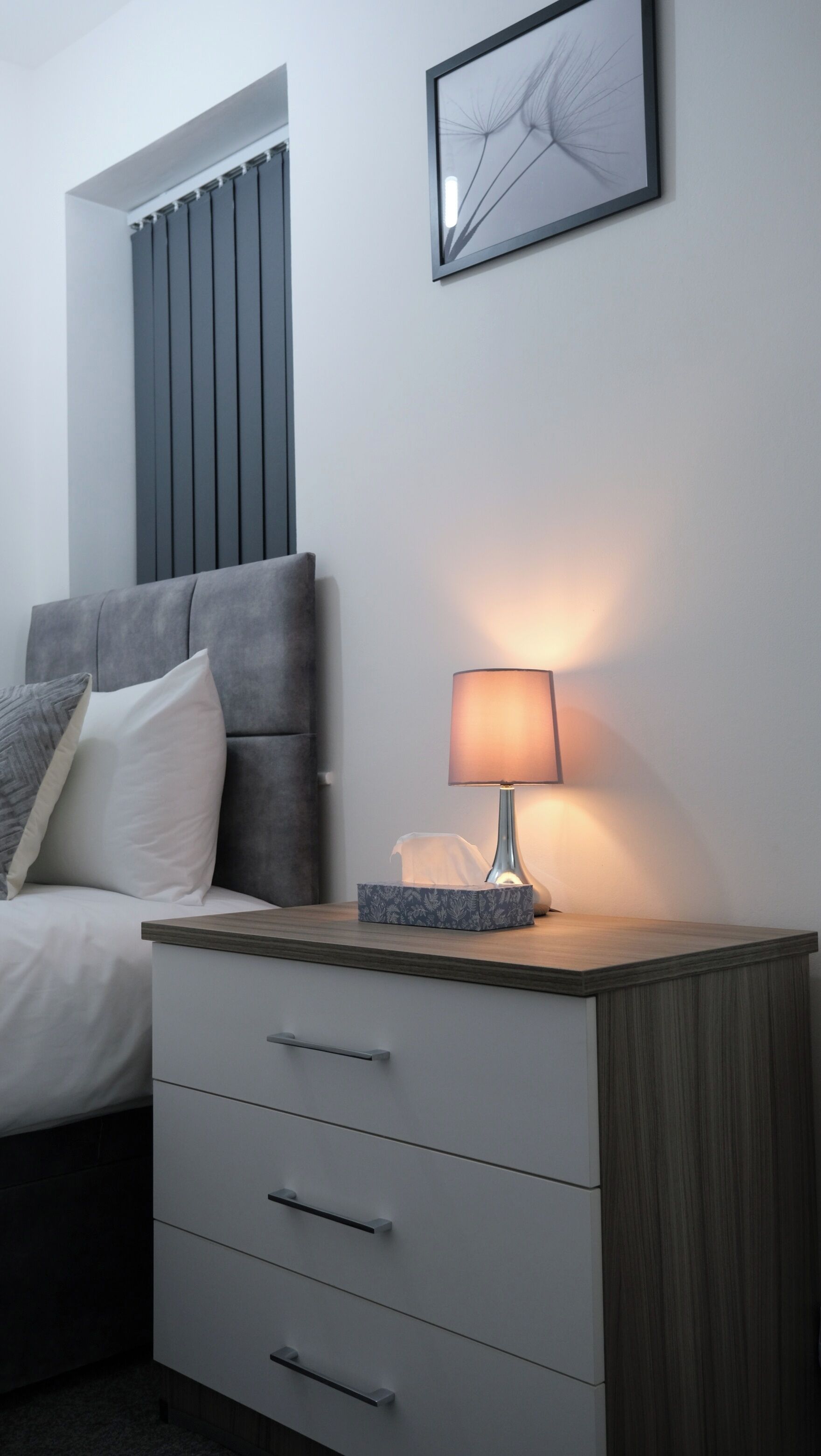 Una camera da letto moderna con un letto, comodino, lampada e un quadro appeso al muro.