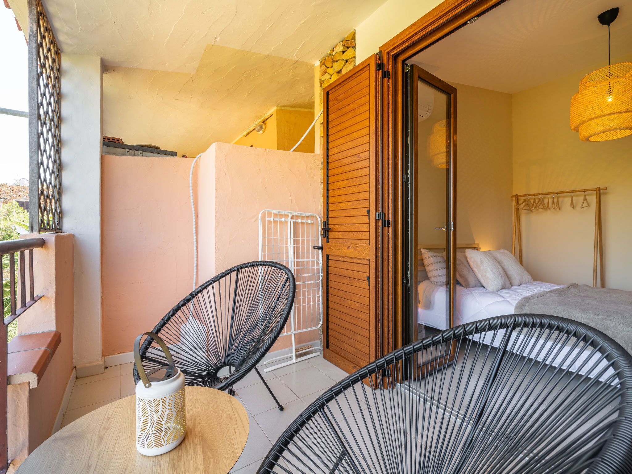 Ein Balkon mit zwei schwarzen Drahtstühlen, einem kleinen Tisch und einer weißen Dekorvase.