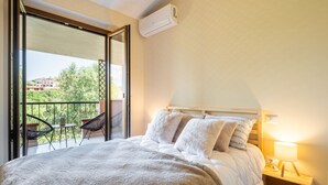 A bedroom with a large bed, a nightstand, a lamp, and a view of a balcony with chairs and a table.