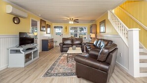 A living room with a television, leather sofas, a coffee table, and a staircase. - Cypress Cottage - Marshfront in Garden City Beach! (Garden City Beach)