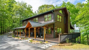 Une cabane en rondins à deux étages, dotée d’un porche couvert et d’un chemin de pierre menant à l’entrée.