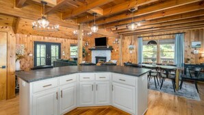 Une cuisine spacieuse avec un grand îlot central, des poutres apparentes en bois au plafond et une cheminée.
