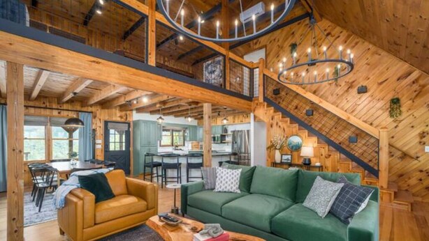 Un vaste espace de vie de style loft, avec un plafond haut, des poutres apparentes, un canapé vert, un fauteuil jaune et une table basse en bois.