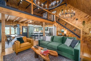 A spacious loft-style room with a high ceiling, wooden beams, a green sofa, a yellow armchair, and a wooden coffee table. - New Listing! Luxury mountain view cabin in the heart of Aska Adventure area (Blue Ridge)
