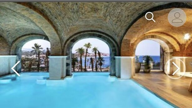 Une piscine intérieure dotée de voûtes et offrant une vue sur les palmiers et la mer.
