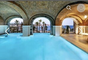 Une piscine intérieure dotée de voûtes et offrant une vue sur les palmiers et la mer.